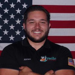 Pacific Heating and Air Conditioning technician Adrian smiling confidently in front of an American flag, representing dedication and professionalism