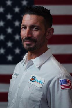 Pacific Heating and Air Conditioning technician in uniform posing in front of an American flag, representing professionalism and dedication.