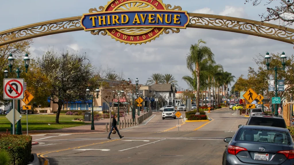 Downtown Chula Vista's Third Avenue archway with palm trees, pedestrians, and parked cars on a sunny day